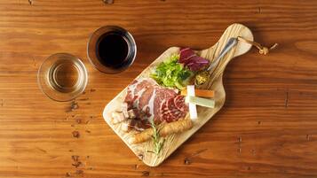 Tábua de madeira com diversos carnes, vegetais e acompanhamentos, acompanhada por dois copos de vinho tinto sobre uma mesa de madeira.