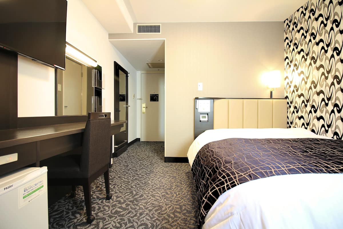 A hotel room with a bed, a desk, a chair, a minibar, and a bathroom.