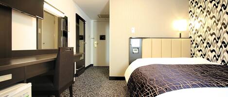 A hotel room with a bed, a desk, a chair, a minibar, and a bathroom.