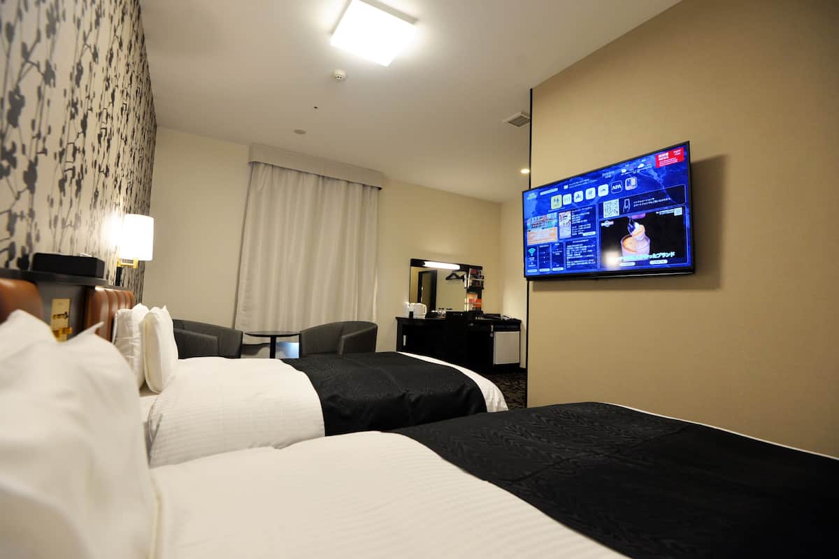 A hotel room with two beds, a desk, a television, and a window with curtains.