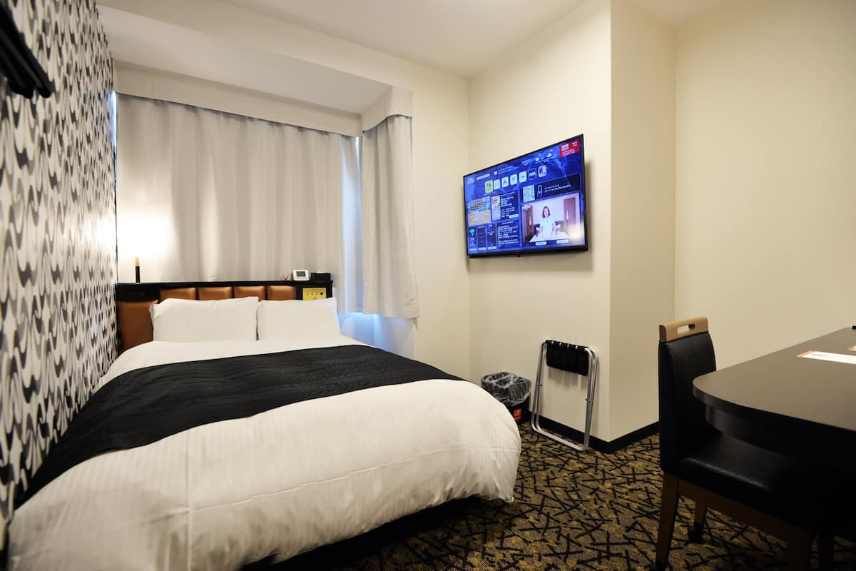 A hotel room with a large bed, a desk, and a television mounted on the wall.