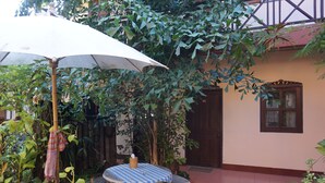 Un patio con una mesa y un banco, rodeado de exuberante vegetación y una casa al fondo.