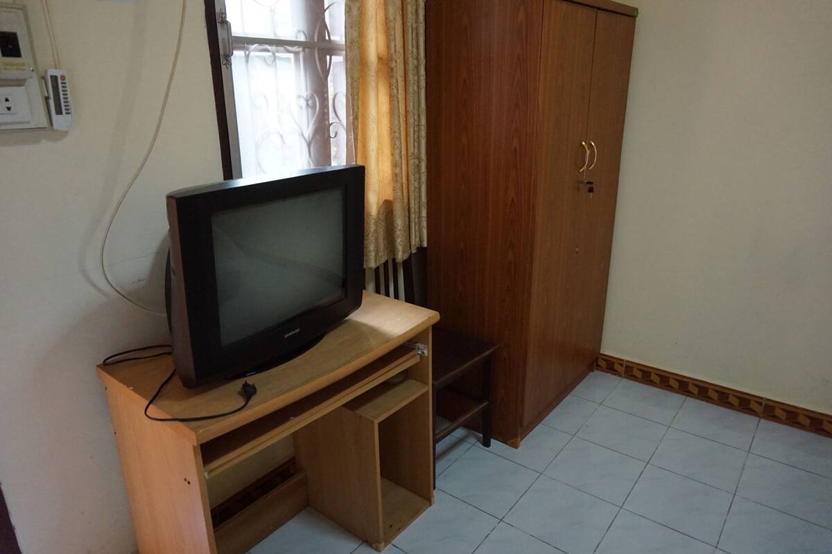 A television on a wooden stand in a room with a wardrobe and a window with curtains.