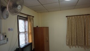 Una habitación con un armario de madera, televisor, ventilador y ventana con cortinas.