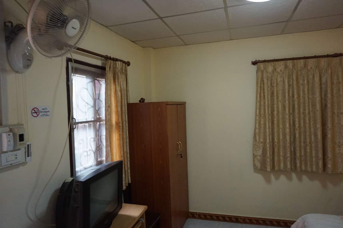 A room with a wooden wardrobe, a television, a fan, and a window with curtains.