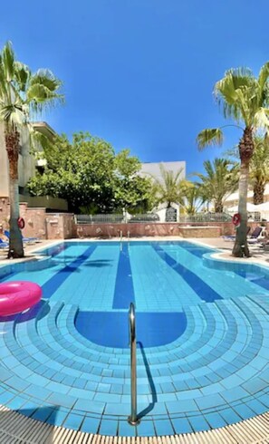 Una piscina al aire libre, sombrillas, sillones reclinables de piscina