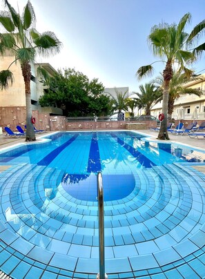 Una piscina al aire libre, sombrillas, sillones reclinables de piscina