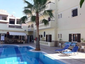 A pool area with lounge chairs and a palm tree. - Semiramis Apartments by Estia (Hersonissos)