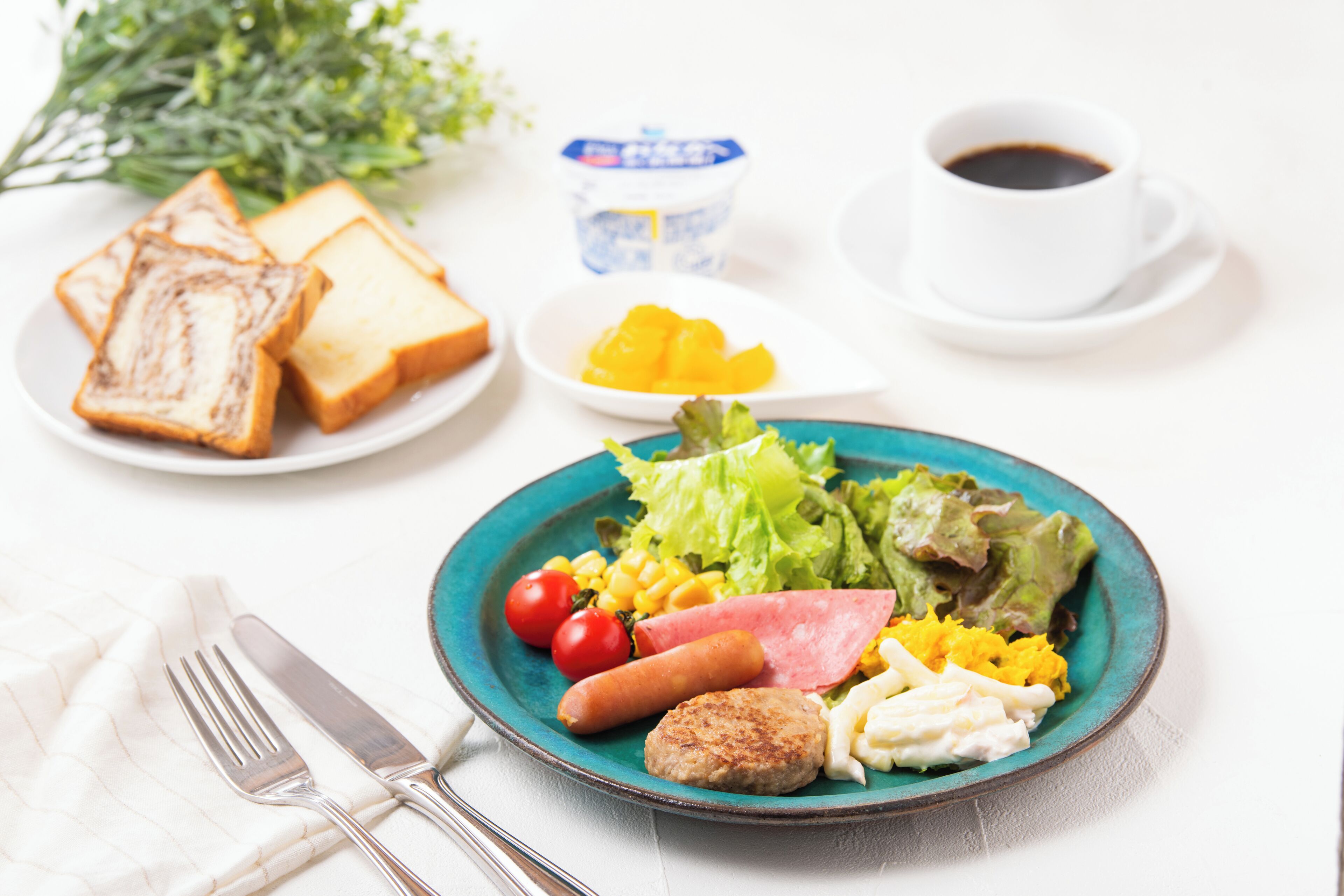 Een ontbijtbord met toast, eieren, tomaten, mais, sla en een worst, vergezeld van een kop koffie en een klein schaaltje fruit.