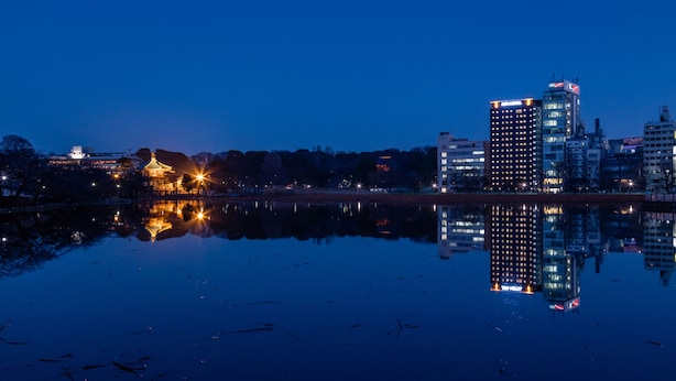 Een stadsgezicht in de schemering, met verlichte gebouwen die rustig in het water worden weerspiegeld.