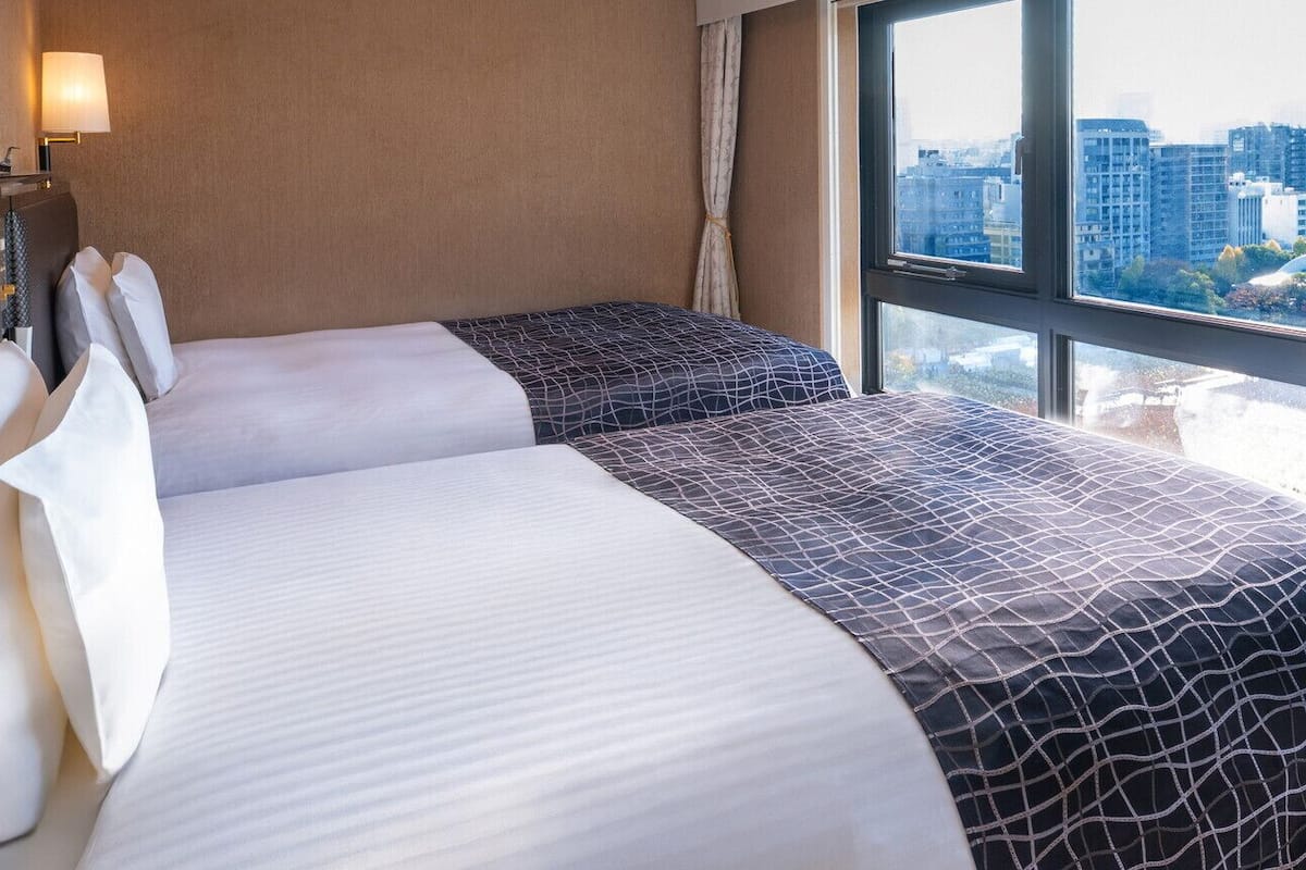 Een hotelkamer met twee bedden, uitzicht over de stad, een lamp en een raam met gordijnen.