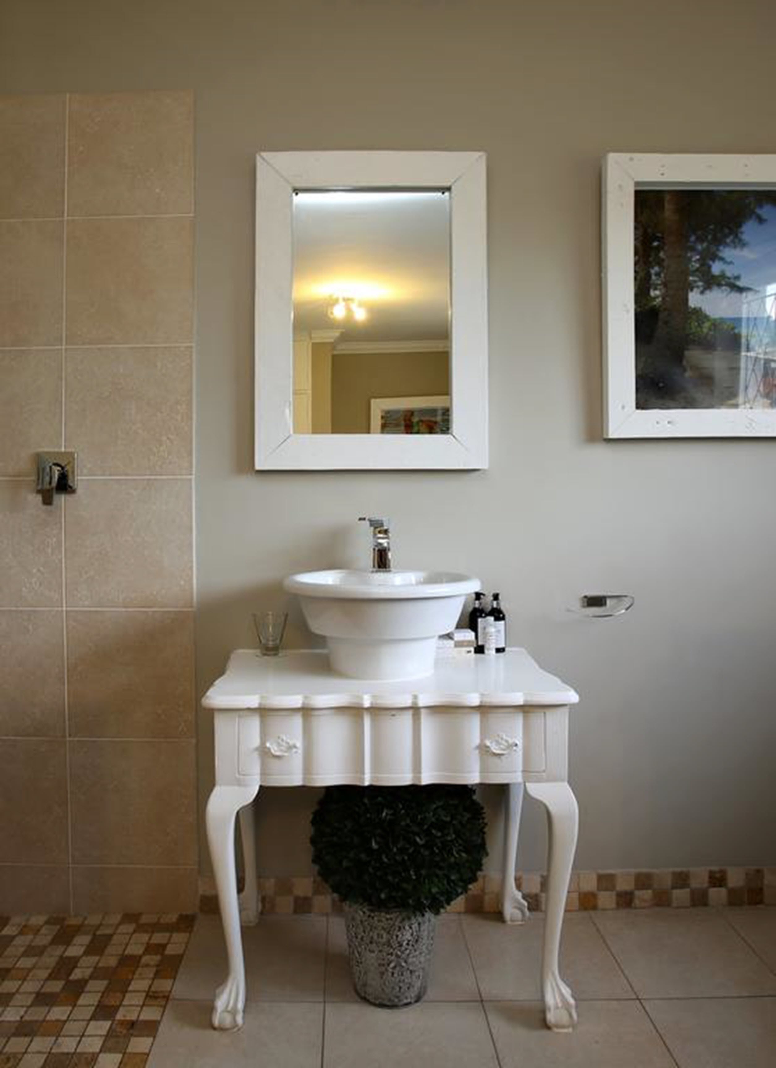 A bathroom with a white vanity, a sink, a mirror, and a potted plant.