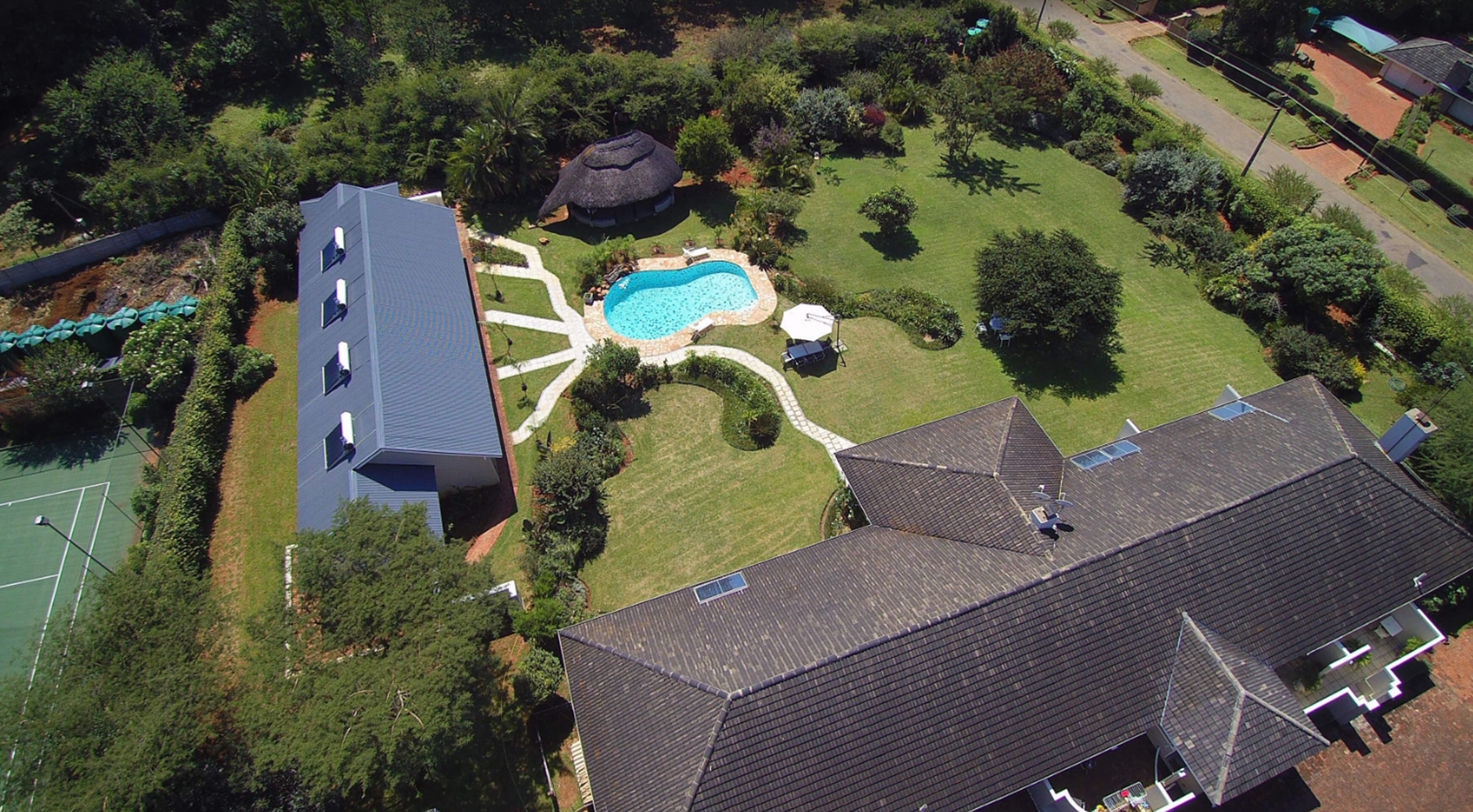 An aerial view of a residential area with a swimming pool, a tennis court, and a large house with a sloped roof.