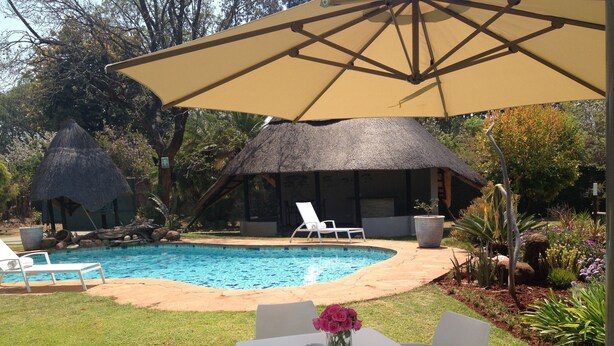 A pool area with a thatched-roof structure, white lounge chairs, and a table with a vase of flowers.