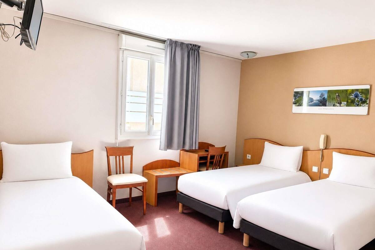 A hotel room with two beds, a desk, a chair, a telephone, and a window with curtains.