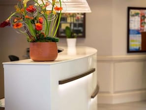 A reception desk with a potted plant and a framed picture on the wall.