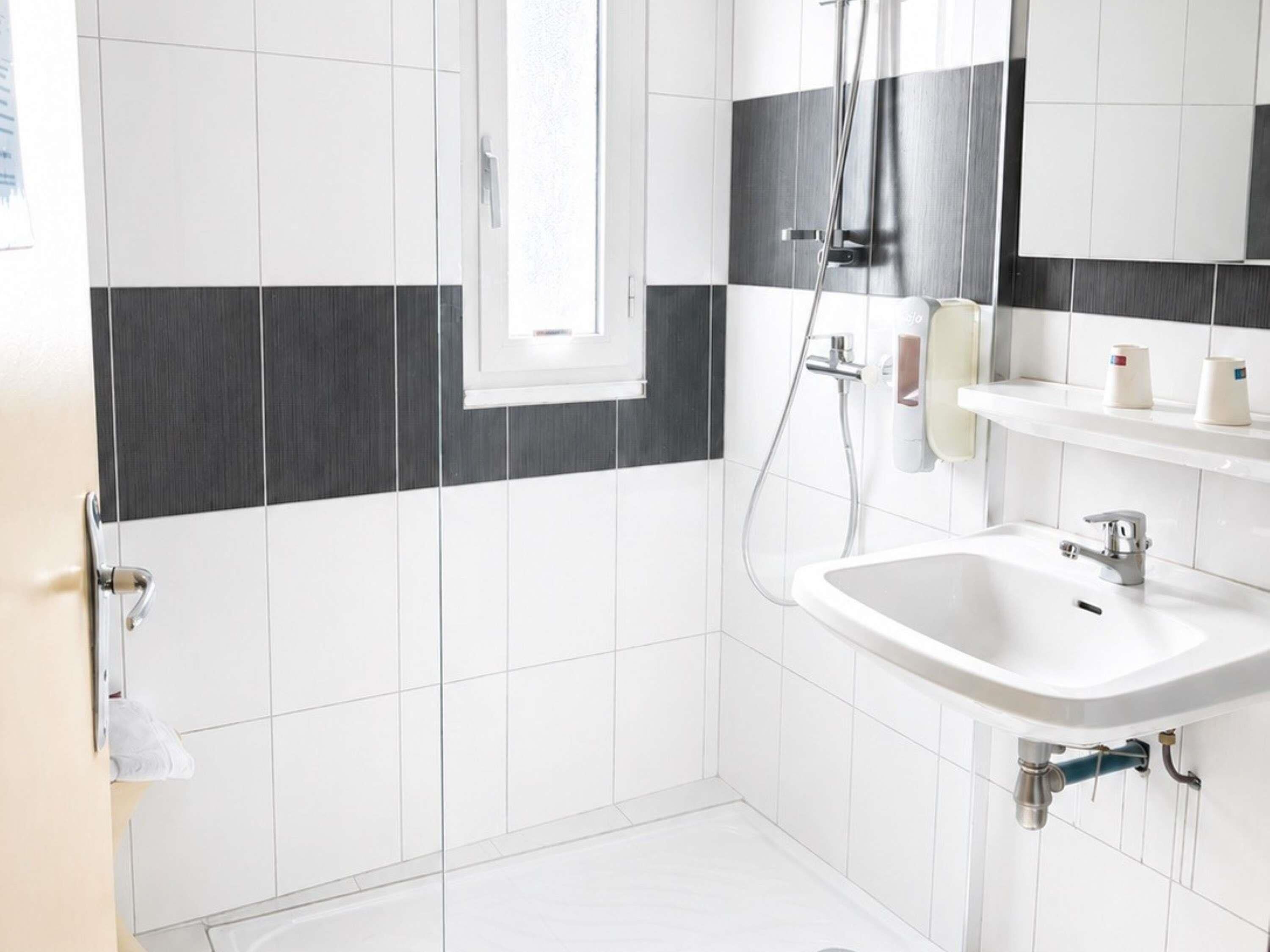 A modern bathroom with white and black tiles, a shower, a sink, and a mirror.