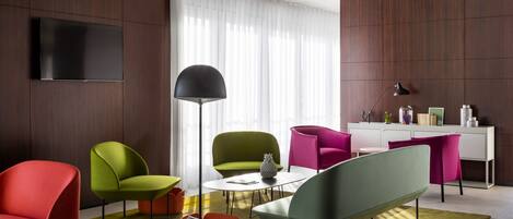 Una sala de estar moderna con un televisor de pantalla plana, una mesa de centro redonda y sillas coloridas.