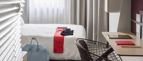 A modern hotel room with a bed, a desk, a chair, and a window with blinds.