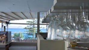 Eine Bar mit Blick auf den Ozean, ein Schild mit der Aufschrift 'NICKERS' und eine Reihe leerer Gläser auf einem Regal.