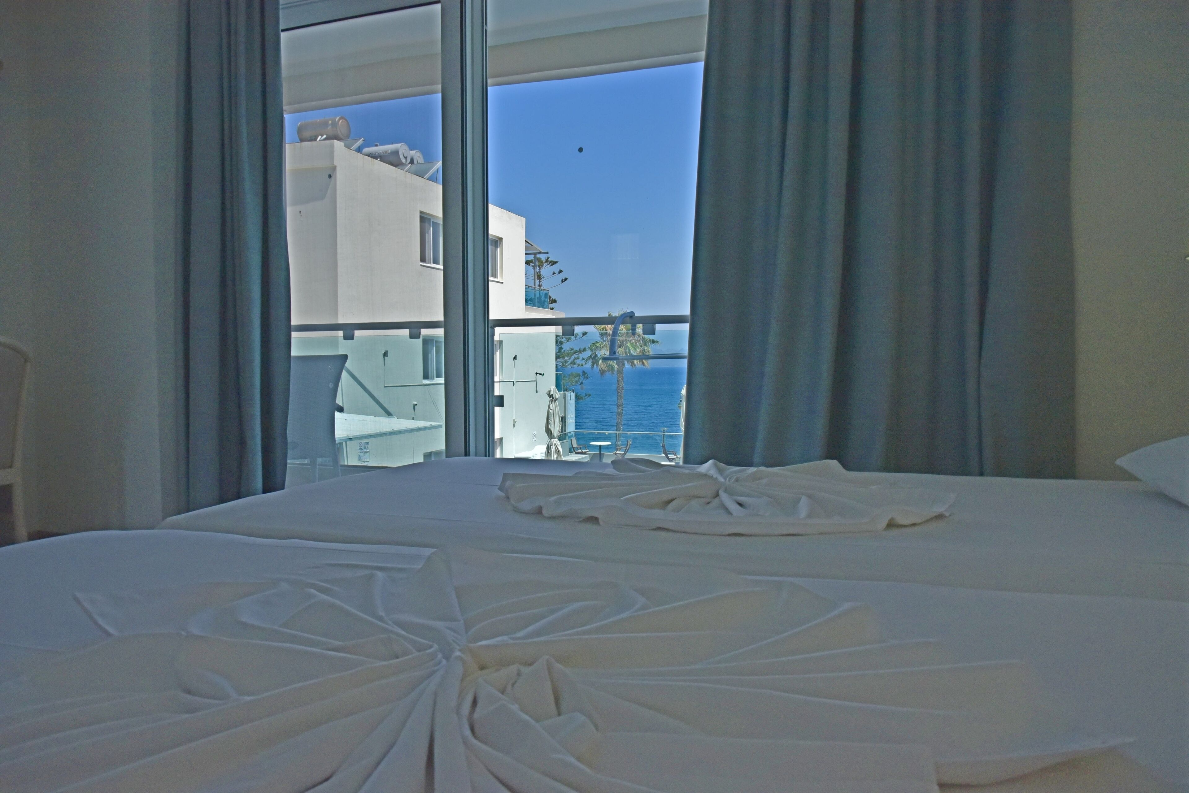 Une chambre d’hôtel avec un grand lit, une vue sur la mer et un bâtiment situé de l’autre côté.