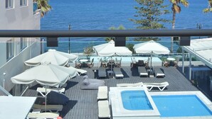 Ein Poolbereich mit Liegestühlen und Sonnenschirmen mit Blick auf das klare, blaue Meer und Land in der Ferne.