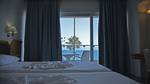 Ein Hotelzimmer mit zwei Betten, Meerblick und einem Balkon mit Tisch und Stühlen.
