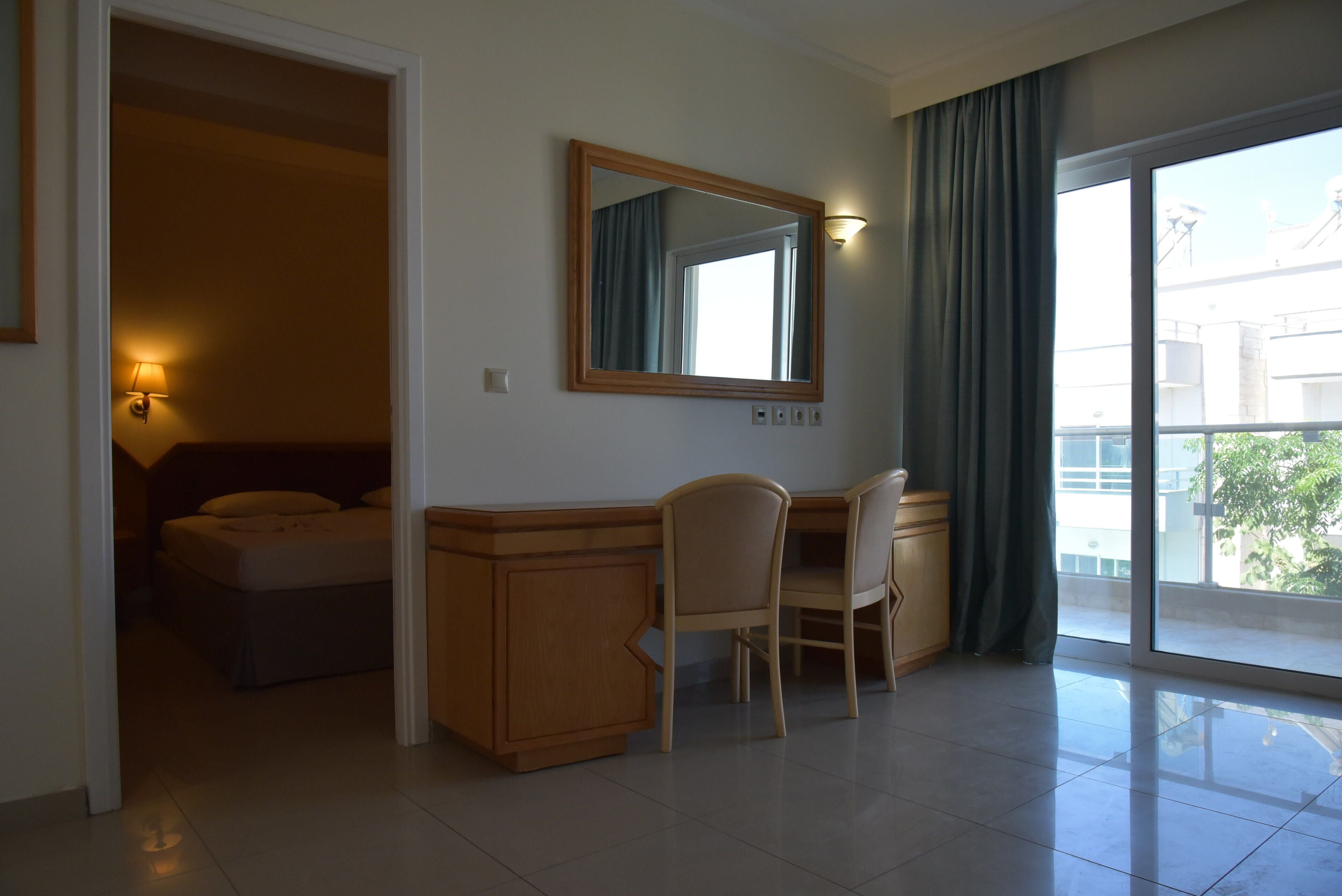 Una camera d'albergo con un letto, una scrivania con una sedia, uno specchio e un'ampia finestra con tende.