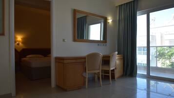 Una camera d'albergo con un letto, una scrivania con una sedia, uno specchio e un'ampia finestra con tende.