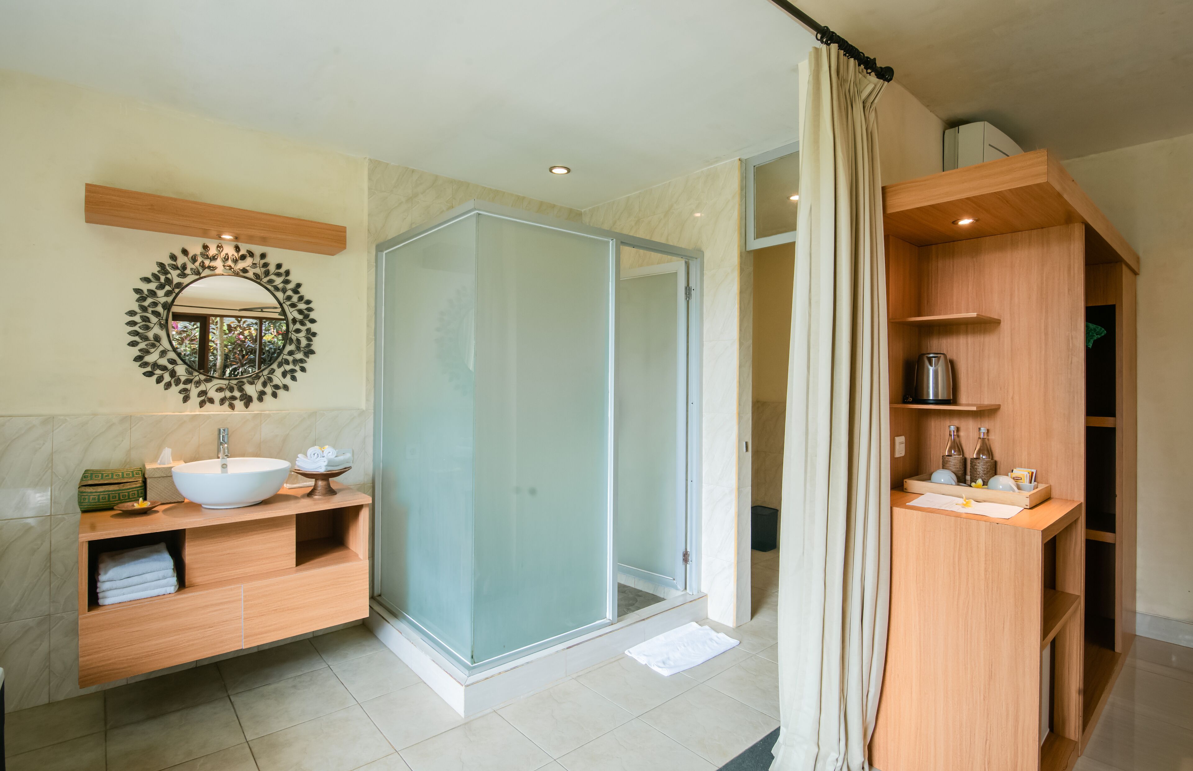 A modern bathroom with a glass-enclosed shower, a wooden vanity with a sink, and a mirror with a leaf design.