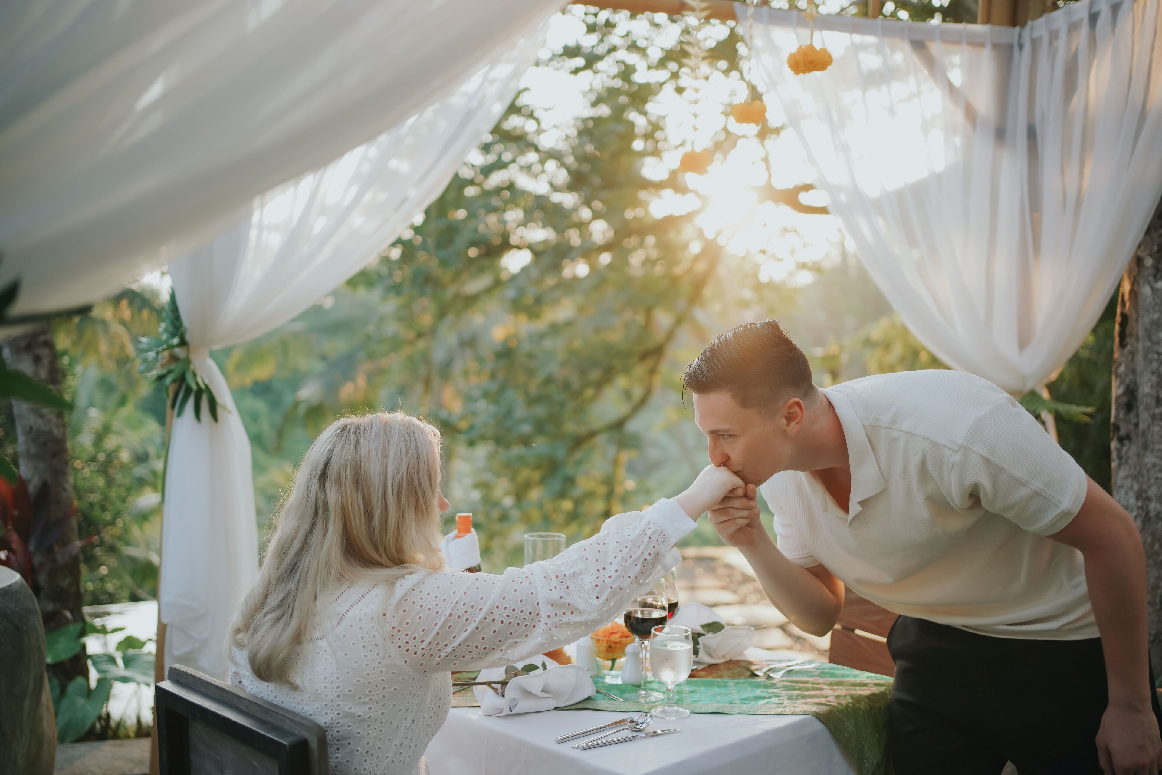A couple dining outdoors with a table set for two, surrounded by greenery.