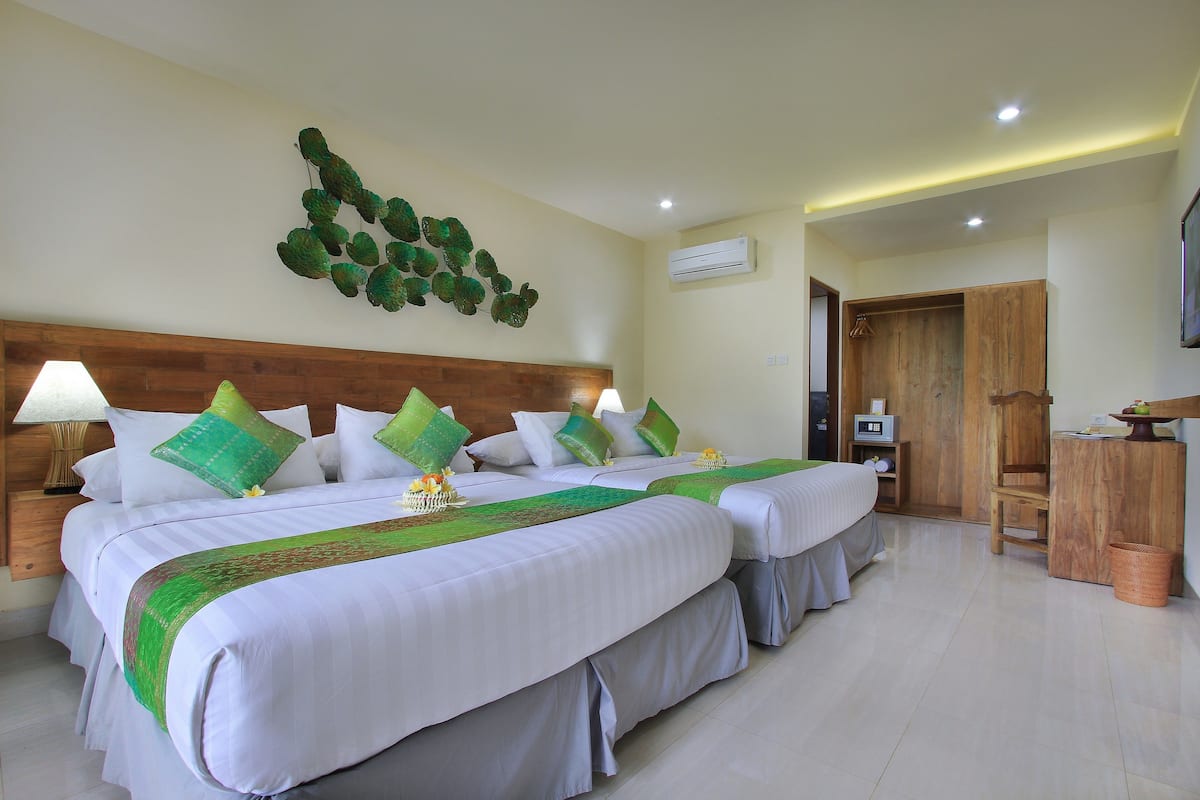 A hotel room with two beds, a wooden headboard, green pillows, a wall-mounted air conditioner, and a wooden cabinet.