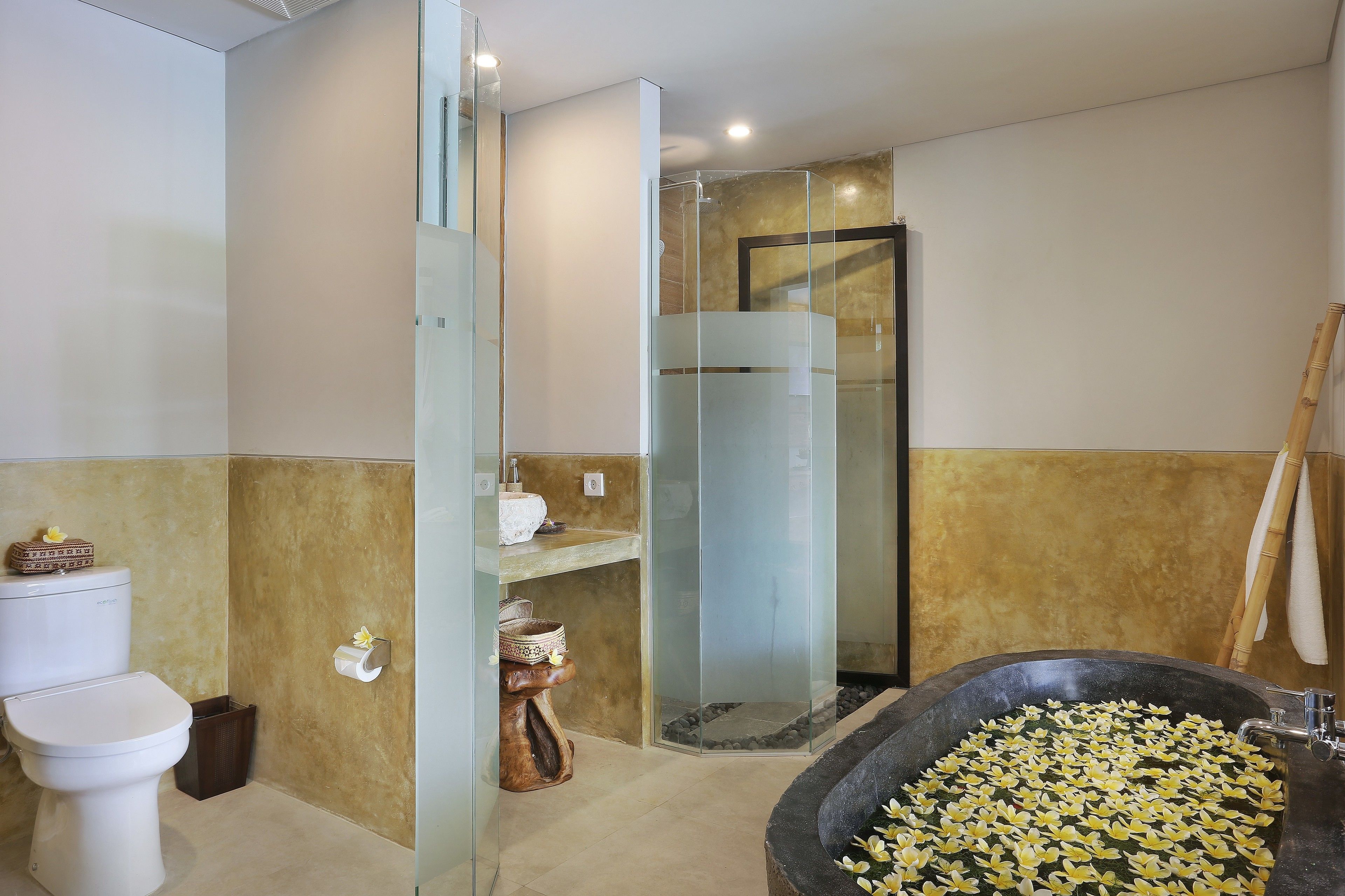 A modern bathroom with a glass-enclosed shower, a large bathtub filled with lotus flowers, and a toilet with a decorative basket.