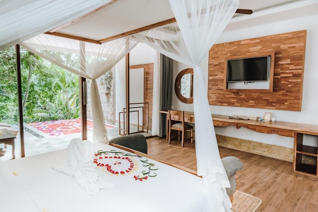 Een slaapkamer met een bed, een bureau, een televisie en uitzicht op groen.