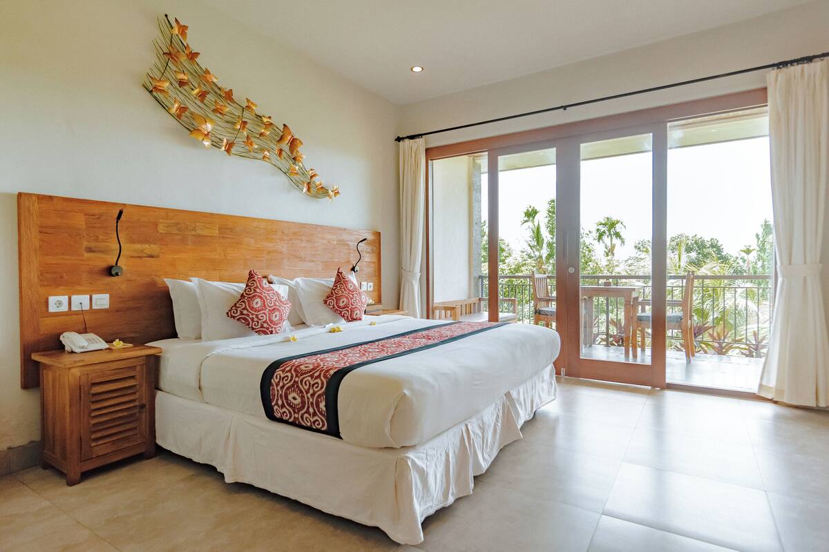 A spacious bedroom with a large bed, a wooden headboard, a nightstand, and a view of the outdoors through a sliding glass door.