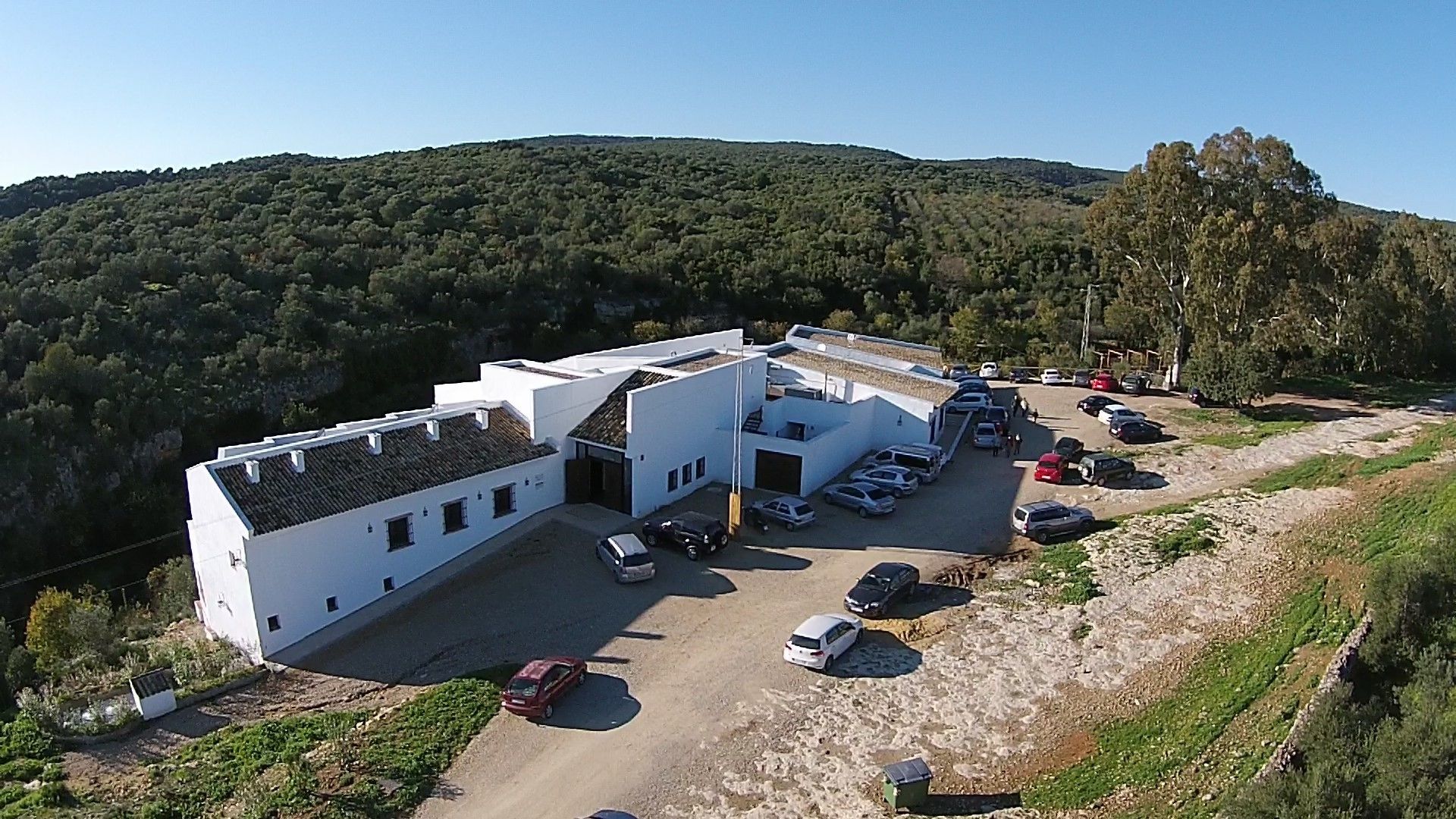 A white building with a parking lot and a hillside in the background.