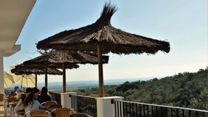 A terrace with thatched umbrellas, wicker furniture, and a view of the countryside. - Centro de Naturaleza Cañada Verde (Hornachuelos)