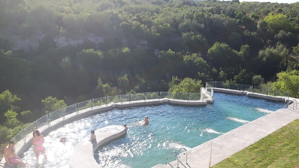 A swimming pool with a curved design, surrounded by a metal fence and a grassy area. - Centro de Naturaleza Cañada Verde (Hornachuelos)