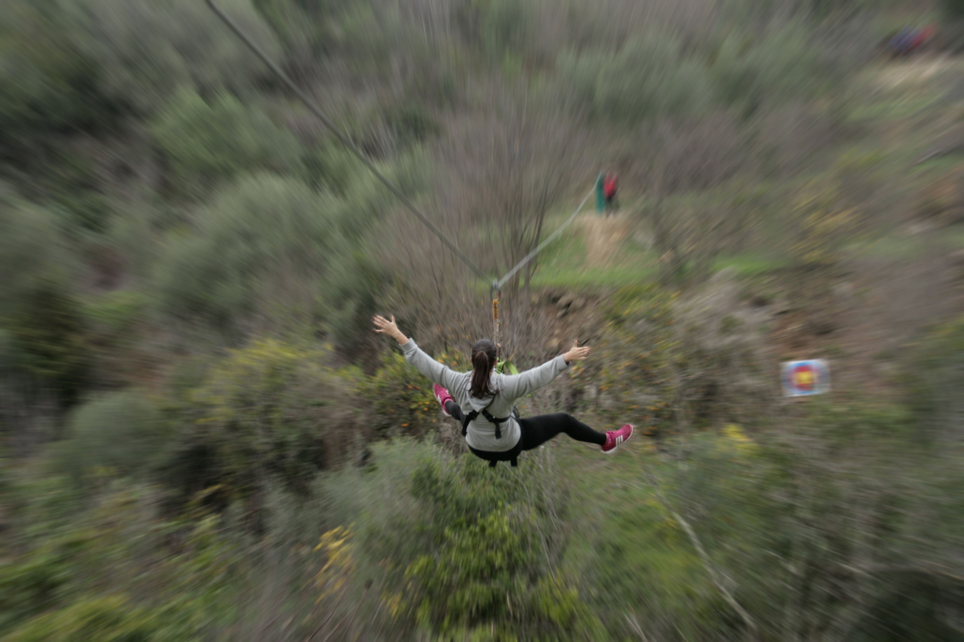 A person bungee jumping with arms outstretched, surrounded by dense vegetation.