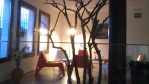 A room with a large window, a red chair, a wooden bench, and a bare tree in the center. - Centro de Naturaleza Cañada Verde (Hornachuelos)