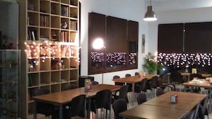 A dining area with multiple tables and chairs, a large bookshelf, and pendant lighting. - Centro de Naturaleza Cañada Verde (Hornachuelos)
