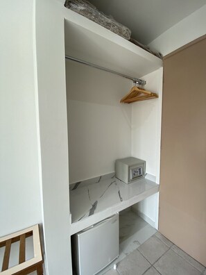 Ein kleines Zimmer mit Einbauschrank, kleinem Kühlschrank und einer Wäscheständer-Konstruktion aus Holz.