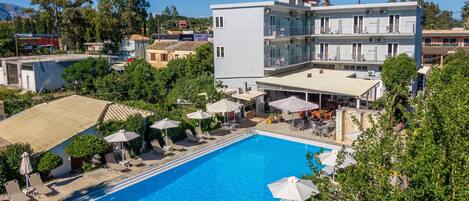 A swimming pool with lounge chairs and umbrellas, surrounded by greenery and buildings.