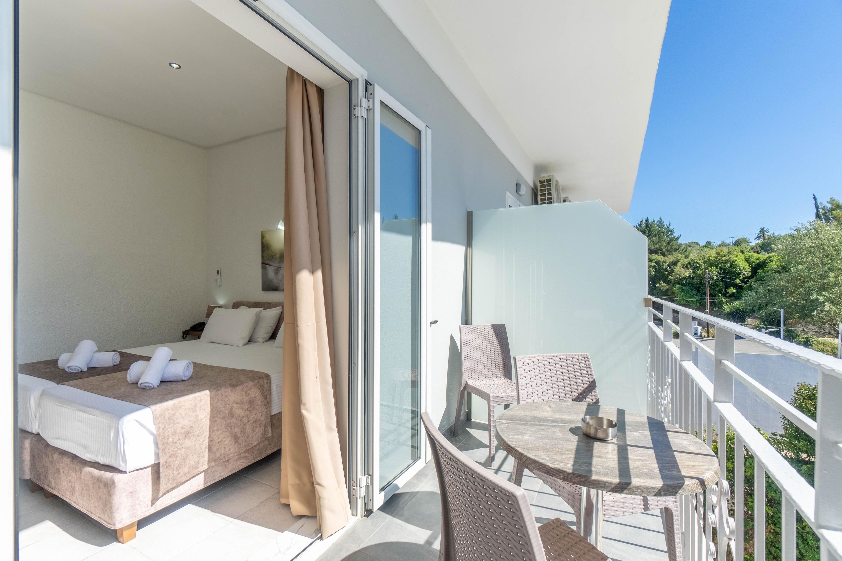 Ein Hotelzimmer mit einem Bett, einem kleinen Tisch mit einer Schale sowie einem Balkon mit Korbstühlen und einem Tisch.