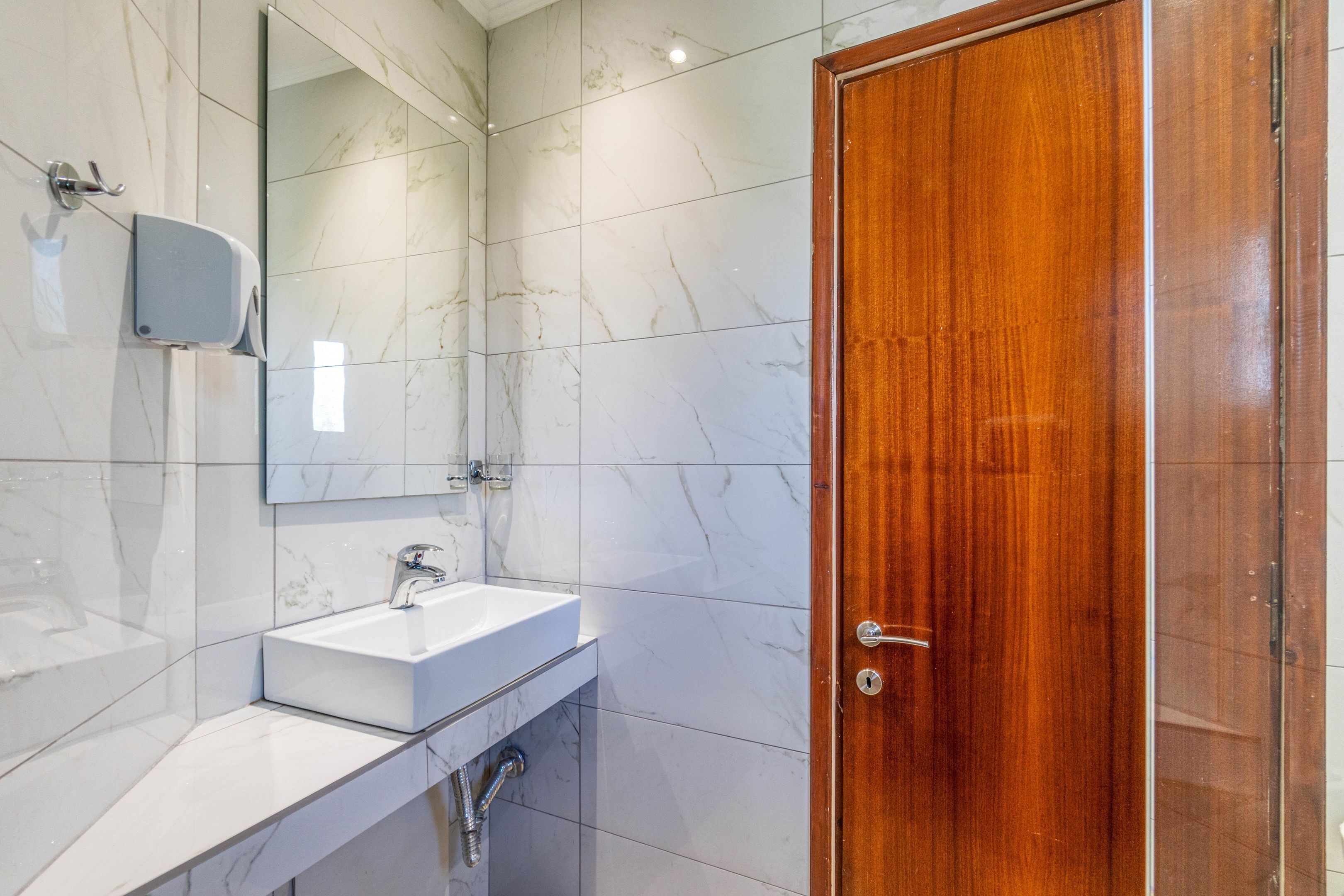 Un baño con lavamanos de mármol blanco, un espejo y una puerta de madera.