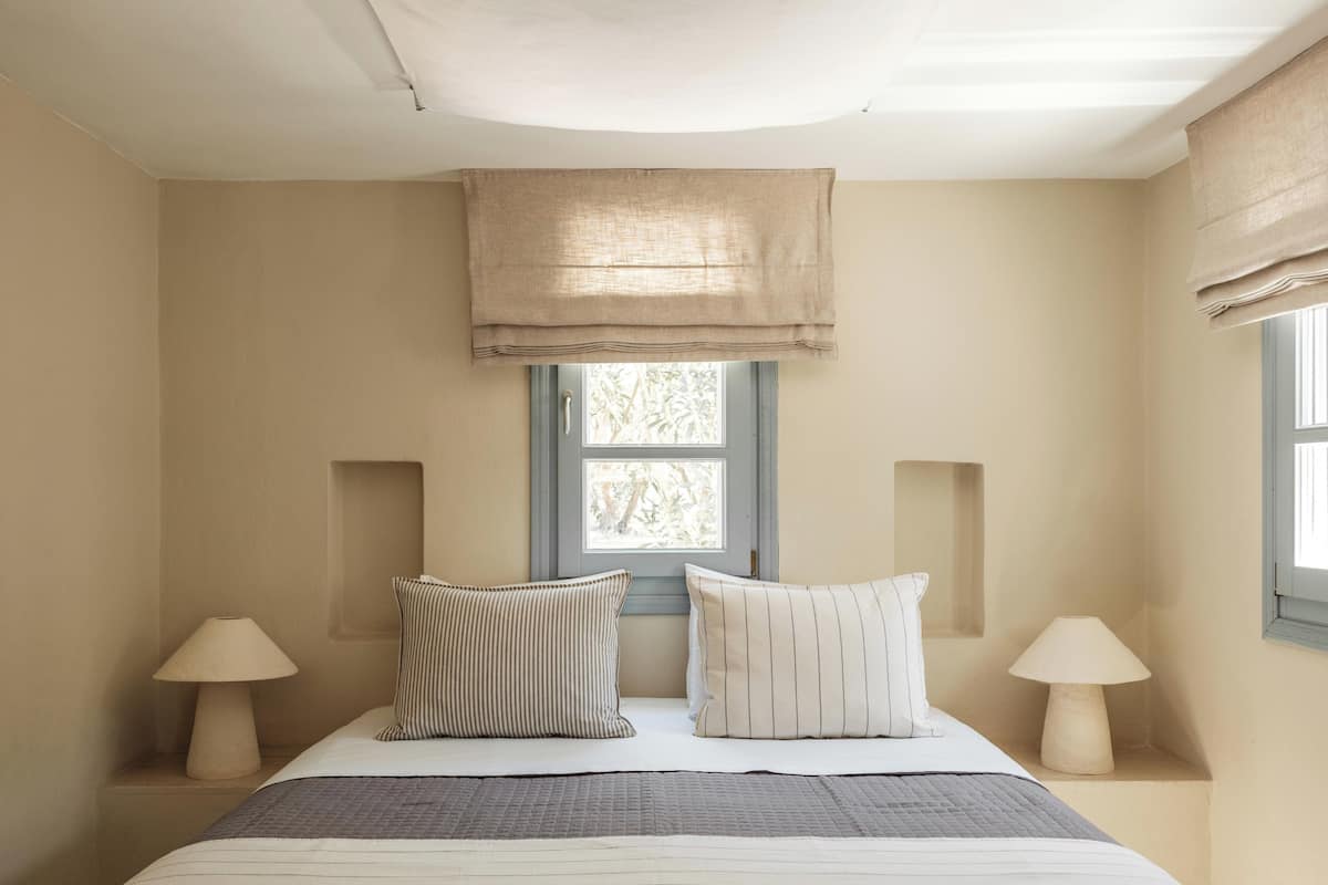 Un dormitorio con cama, dos lámparas de noche, ventana con vistas y lámpara en el techo.