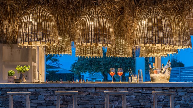 A bar area with stone walls, wooden chairs, and a thatched ceiling with hanging lights. - Verina Terra (Sifnos)