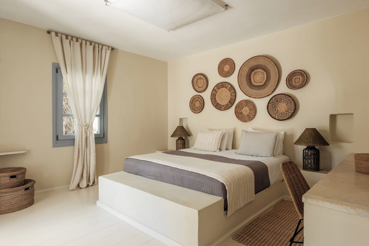Un dormitorio con cama, mesitas de noche, una silla, una ventana con cortinas y decoración en la pared.