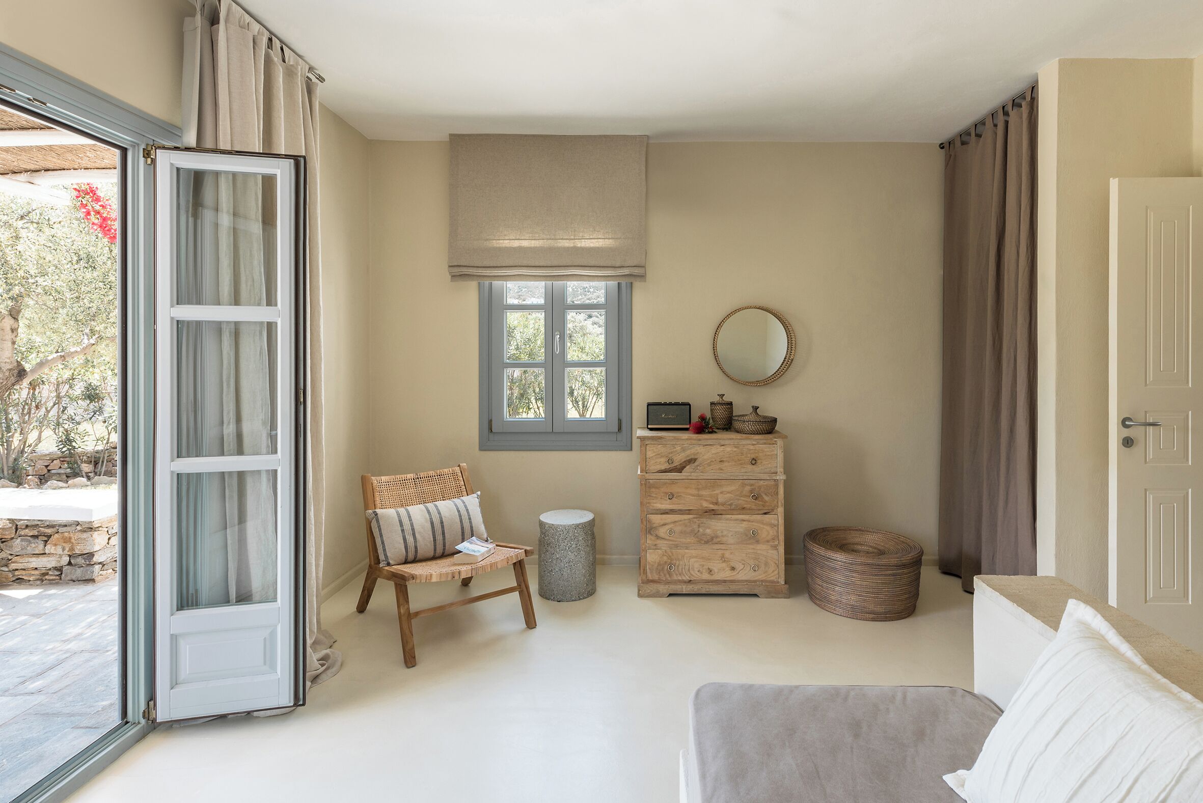 Ein Schlafzimmer mit einem Bett, einem Sessel, einem Schminktisch und einem runden Spiegel sowie einem Fenster.