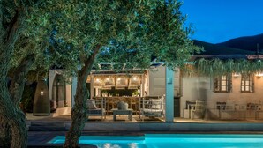 A poolside area with a bar and seating, surrounded by trees and a building with a thatched roof. - Verina Terra (Sifnos)
